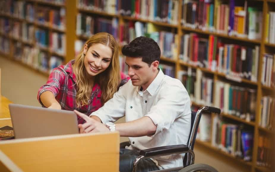 Deux étudiants dans une bibliothèque, dont un en fauteuil.