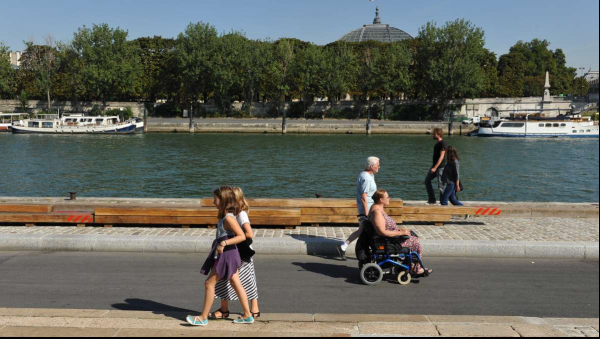 Photo d'une rue au bord de l'eau ou se croisent un couple avec une femme en fauteuil et deux enfants