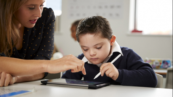 Enfant travaillant sur une tablette, aidé d'une professeure des écoles.