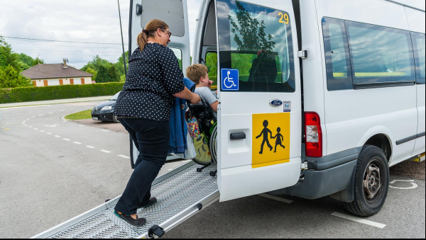 Conductrice d'un minibus faisant rentrer un enfant en fauteuil dans ce dernier.