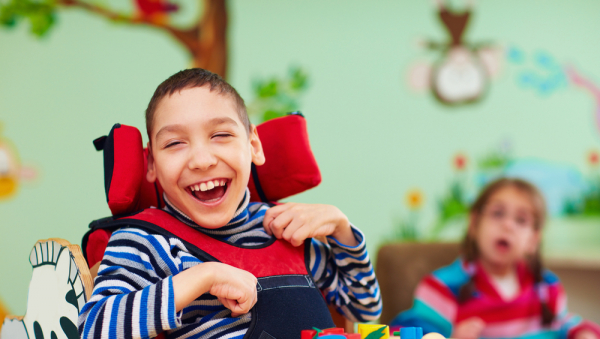 Enfant en fauteuil dans une salle de classe souriant.